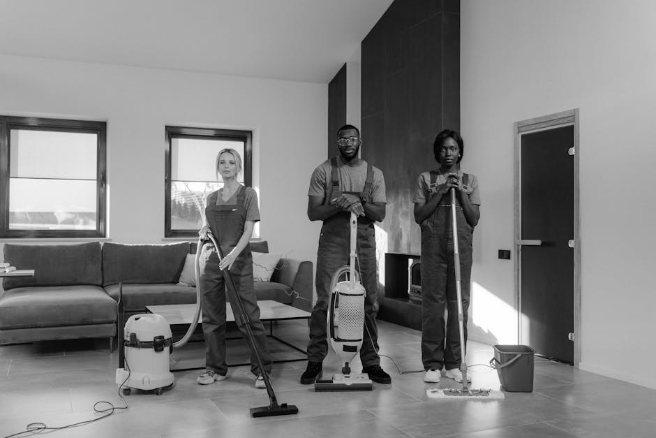 A person kneeling on a patterned carpet while using a yellow and black vacuum cleaner for surface cleaning and deep cleaning. The individual is wearing a beige jacket and blue jeans, and appears to be